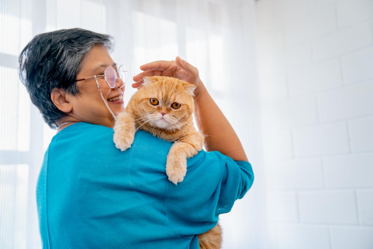 Mature woman smiles and pets her yellow cat as he lounges on her shoulder