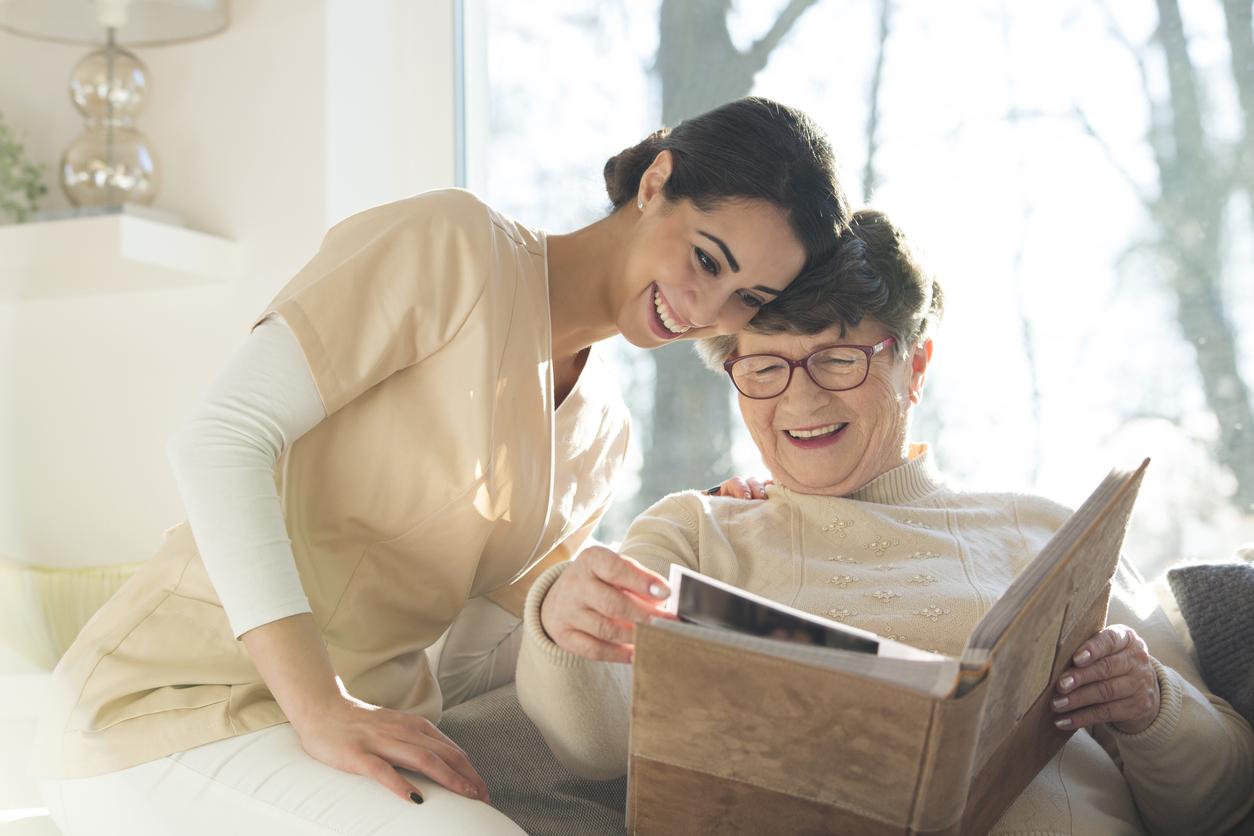 Senior in memory care shares photo album with caregiver, smiling and reliving memories